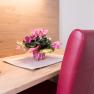 Double room, © W. Garhöfer A desk with a remote control, a bouquet of flowers and a red chair.