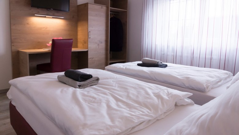 Double room, © W. Garhöfer Twin room with two beds, desk, chair and closet. Towels on the beds, window with curtains in the background.