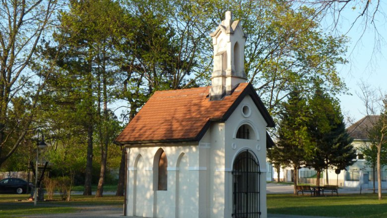 Gedenkkapelle, © Werner Ertl Eine kleine weiße Kapelle mit rotem Dach in einem Park, umgeben von Bäumen.