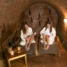 Winery Küssler, © Winzerhof Küssler Two women in white bathrobes relax on loungers in a wine cellar with brick walls.