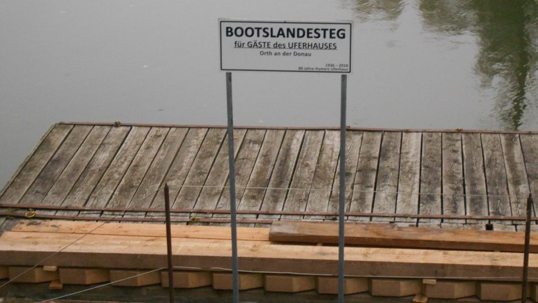 Bootsanlegestelle, © Humers Uferhaus Holzsteg mit Schild 'Bootslandesteg für Gäste des Uferhauses' an einem ruhigen Gewässer.