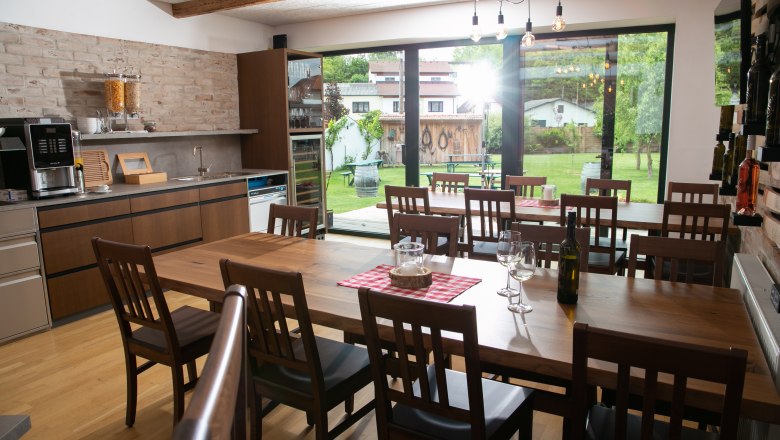 Winzerhof Küssler, © Winzerhof Küssler Innenansicht eines modernen Gastraums mit Holztischen und Stühlen, großen Fenstern und Blick auf einen Garten.