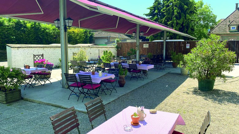 Gastgarten, © Andreas Sinnhuber Ein Gastgarten mit Tischen und Stühlen unter einem Sonnenschutz, umgeben von Pflanzen.