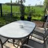 Sitzgelegenheit im Garten, © Dana Perl Gartentisch mit Stühlen auf einer Terrasse, umgeben von grünem Rasen und einem Zaun.