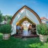 Winery Küssler, © Winzerhof Küssler A tent with a wooden structure on a meadow where people are sitting at tables. In front of the tent are large planters with flowers.