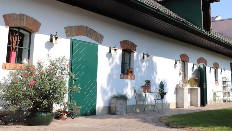 Beerenhof Prenner, © Trixi Rollin Ein weißes Gebäude mit grünen Türen und Fenstern, umgeben von Pflanzen und Gartenmöbeln.