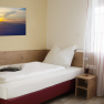 Single room, © W. Garhöfer A simple single room with a bed, a bedside table and a picture on the wall. A window with curtains lets in light.