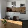 Amber Motel, © Bernstein Motel Modern kitchen unit with white cupboards, wooden worktop, coffee machine and microwave. A table with a bouquet of flowers in the foreground.