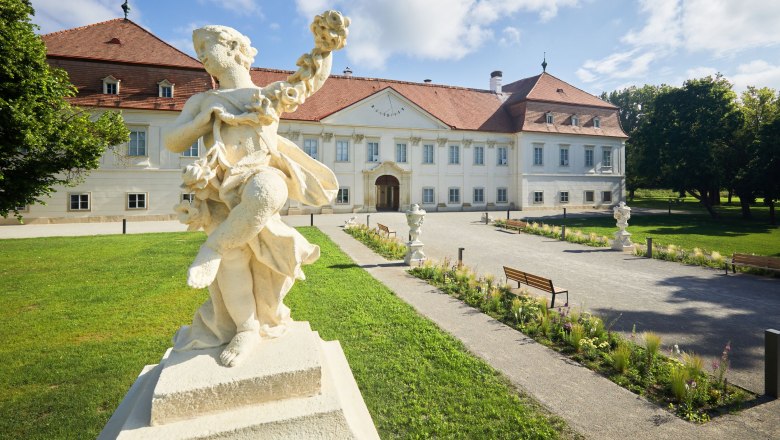 Schloss Marchegg, © RupertPessl Barocke Statue vor einem historischen Gebäude mit rotem Dach und gepflegtem Garten.