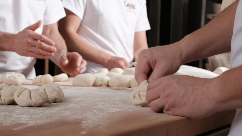 Bakers form dough on a floured table.