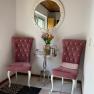 An anteroom with two pink chairs, a round mirror and a small table with flowers.