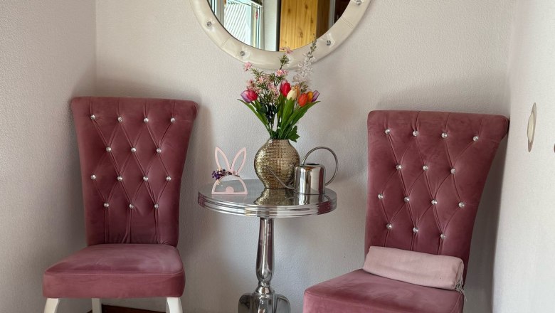 Ein Vorraum mit zwei rosa Stühlen, einem runden Spiegel und einem kleinen Tisch mit Blumen.