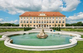 Schloss Hof mit Brunnen im Vordergrund und Gartenanlage.