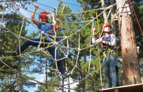 Two people climbing in a high ropes course with safety equipment.