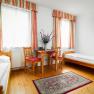 Ein einfach eingerichtetes Zimmer mit zwei Einzelbetten, einem Tisch mit zwei Stühlen, einem Teppich und einem Fernseher an der Wand.