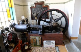 Alte Dampfmaschine im Museum mit Werkzeugen und Warnschild.