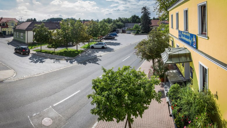 Straßenszene mit gelbem Gebäude und Parkplatz, Bäume und Autos.