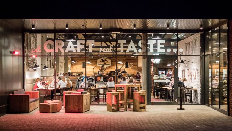 Exterior view of a restaurant with a glass front, inside people are sitting at tables.