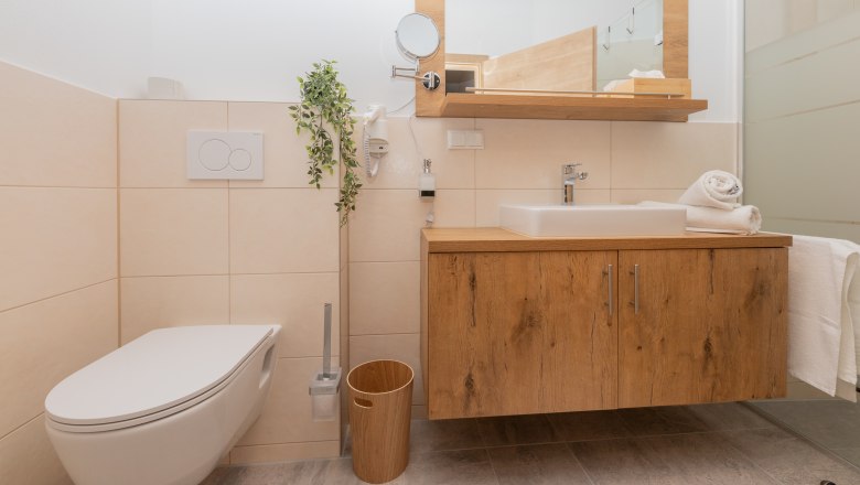 Modernes Badezimmer mit Holzwaschtisch, Waschbecken, Toilette und Handtüchern.