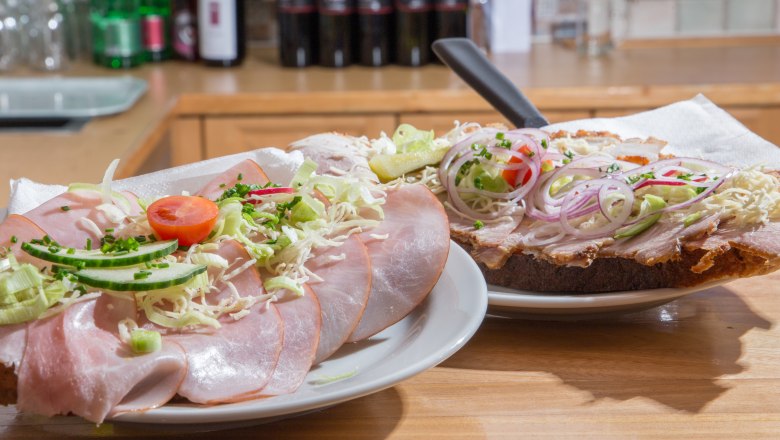 Zwei belegte Brote mit Schinken, Zwiebeln und Gemüse auf einem Tisch.