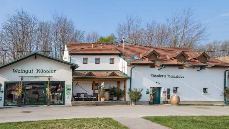 Weingut K&uuml;ssler with wine bar and terrace, surrounded by trees.