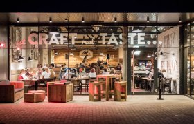 Außenansicht eines Restaurants mit Glasfront und Holzmöbeln.