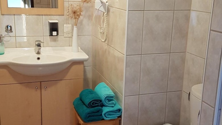 Ein Badezimmer mit Waschbecken, Spiegel, Toilette und Handtüchern auf einem Hocker.