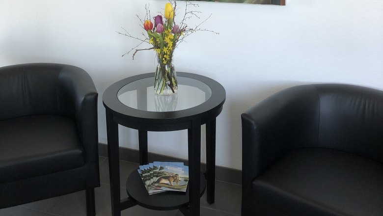 Two black armchairs and a round table with flowers in a room. An abstract painting with a fox motif hangs on the wall.