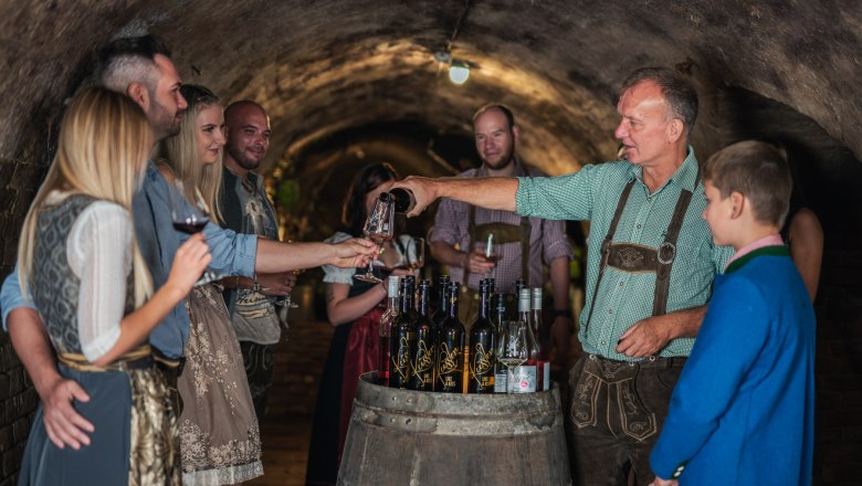 A group of people in traditional dress at a wine tasting in a wine cellar.