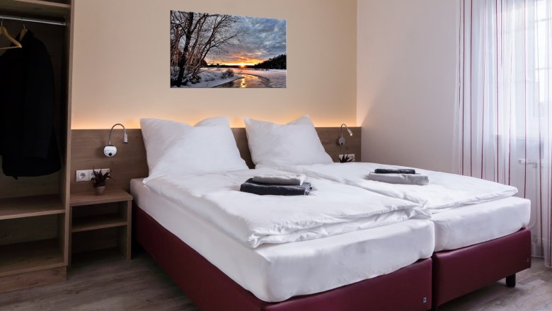 Modernes Doppelzimmer mit zwei Einzelbetten, Bild an der Wand, Kleiderschrank und Fenster mit Vorhängen.