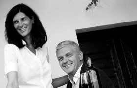 Schwarz-Wei&szlig;-Foto eines l&auml;chelnden Paares mit Weinflasche.