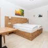 Modernes Schlafzimmer mit Holzm&ouml;beln, Doppelbett, Tisch und Stuhl. Ein Spiegel und Bilder an der Wand, T&uuml;r f&uuml;hrt zu einem Badezimmer.