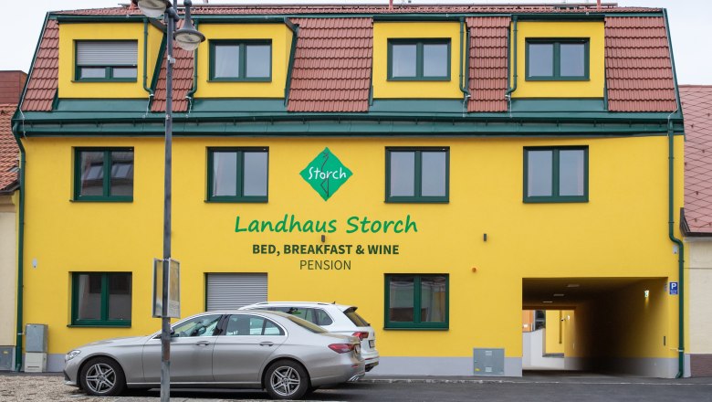 Gelbes Gebäude mit der Aufschrift 'Landhaus Storch', davor geparkte Autos.