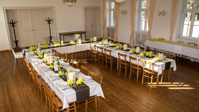 Festively decorated event hall with long tables and yellow napkins.