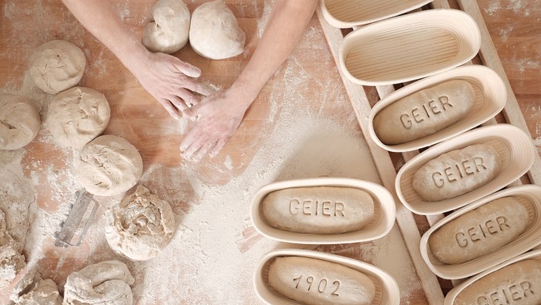 Hände formen Teig auf bemehltem Tisch, daneben Gärkörbe mit "GEIER" und "1902".
