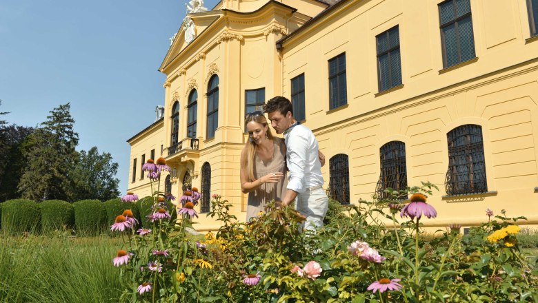 Ein Paar steht vor Schloss Eckartsau, umgeben von einem blühenden Garten.