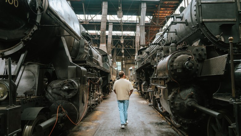 Person walking between two old steam locomotives in a hall.