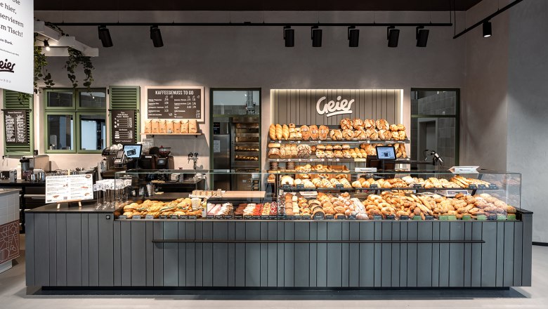 Innenansicht einer modernen Bäckerei mit einer Theke voller Backwaren und einem Schild mit dem Namen Geier.