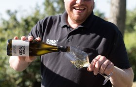 Mann schenkt Wein in ein Glas im Freien ein.