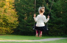 Ein Kind schaukelt in einem Park, umgeben von gr&uuml;nen B&auml;umen.