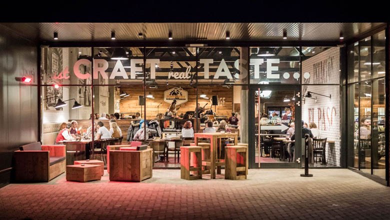 Au&szlig;enansicht eines Restaurants mit Glasfront und Holzm&ouml;beln.