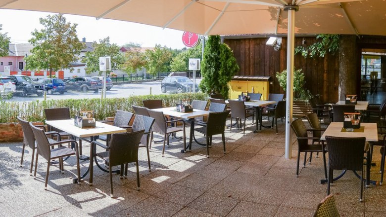 A sunny guest garden with empty tables and chairs, surrounded by plants and a large parasol.