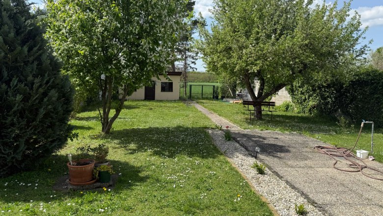 Ein grüner Garten mit Bäumen, einem Weg und einem kleinen Gebäude im Hintergrund.