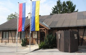 Entrance to the Strasshof museum of local history with two flagpoles and a wooden fence.