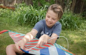 Ein Kind sitzt im Gras und h&auml;lt einen bunten Drachen in den H&auml;nden.