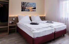 Modernes Doppelzimmer mit zwei Einzelbetten, Bild an der Wand, Kleiderschrank und Fenster mit Vorh&auml;ngen.