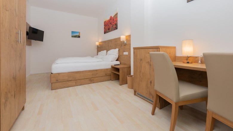 Modernes Schlafzimmer mit Holzm&ouml;beln, Doppelbett, Schreibtisch und Flachbildfernseher.