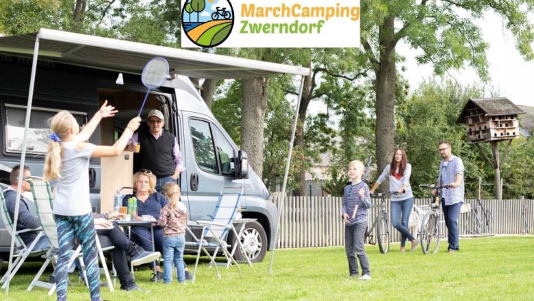 Familie beim Camping mit Wohnmobil und Badmintonspiel auf einer Wiese.