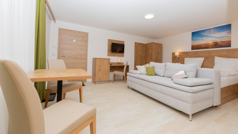 Modernes Schlafzimmer mit Schlafsofa, Tisch und Stühlen, Holzmöbeln und Landschaftsbild an der Wand.