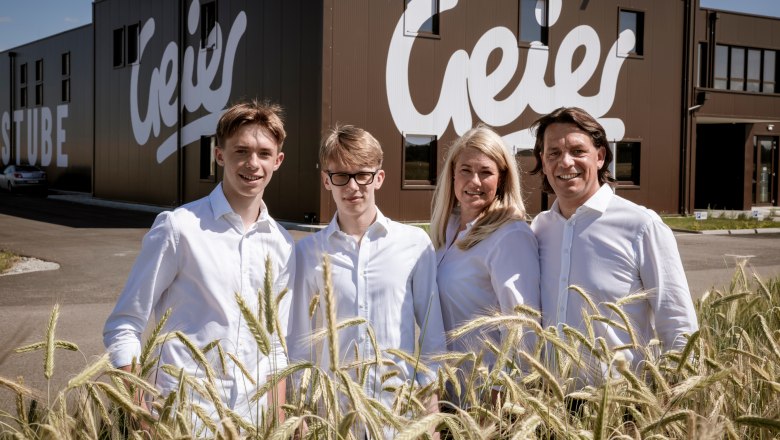 Four people in white clothing are standing in front of a building with the sign 'Geier'.